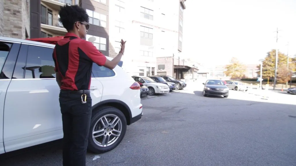 A parking attendant guiding a driver to the valet.