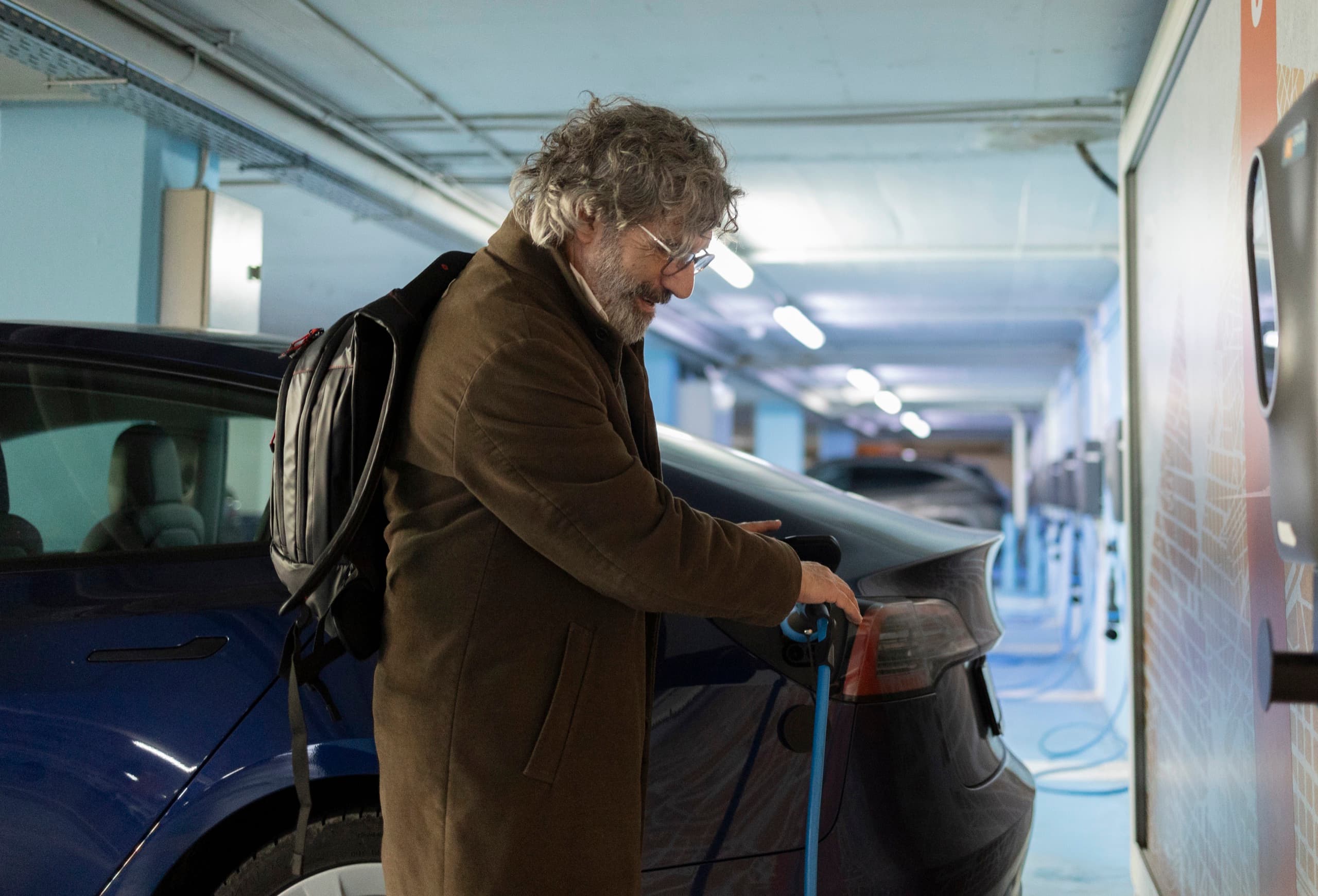 Driver charging an electric vehicle at a parking facility.